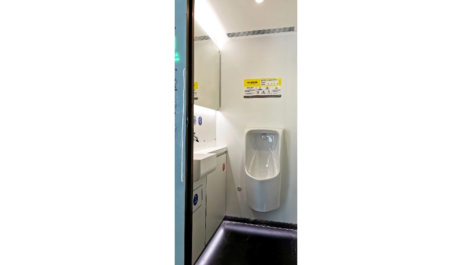 Urinal and wash-basin interior inside a compact public toilet module